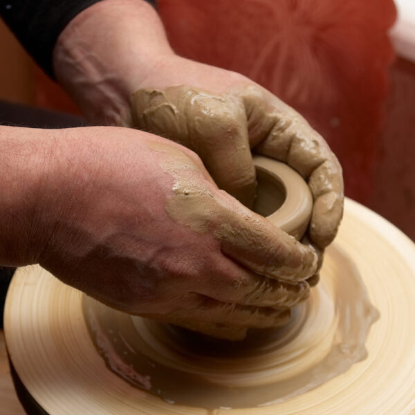 Two hands making a small pot on a pottery wheel