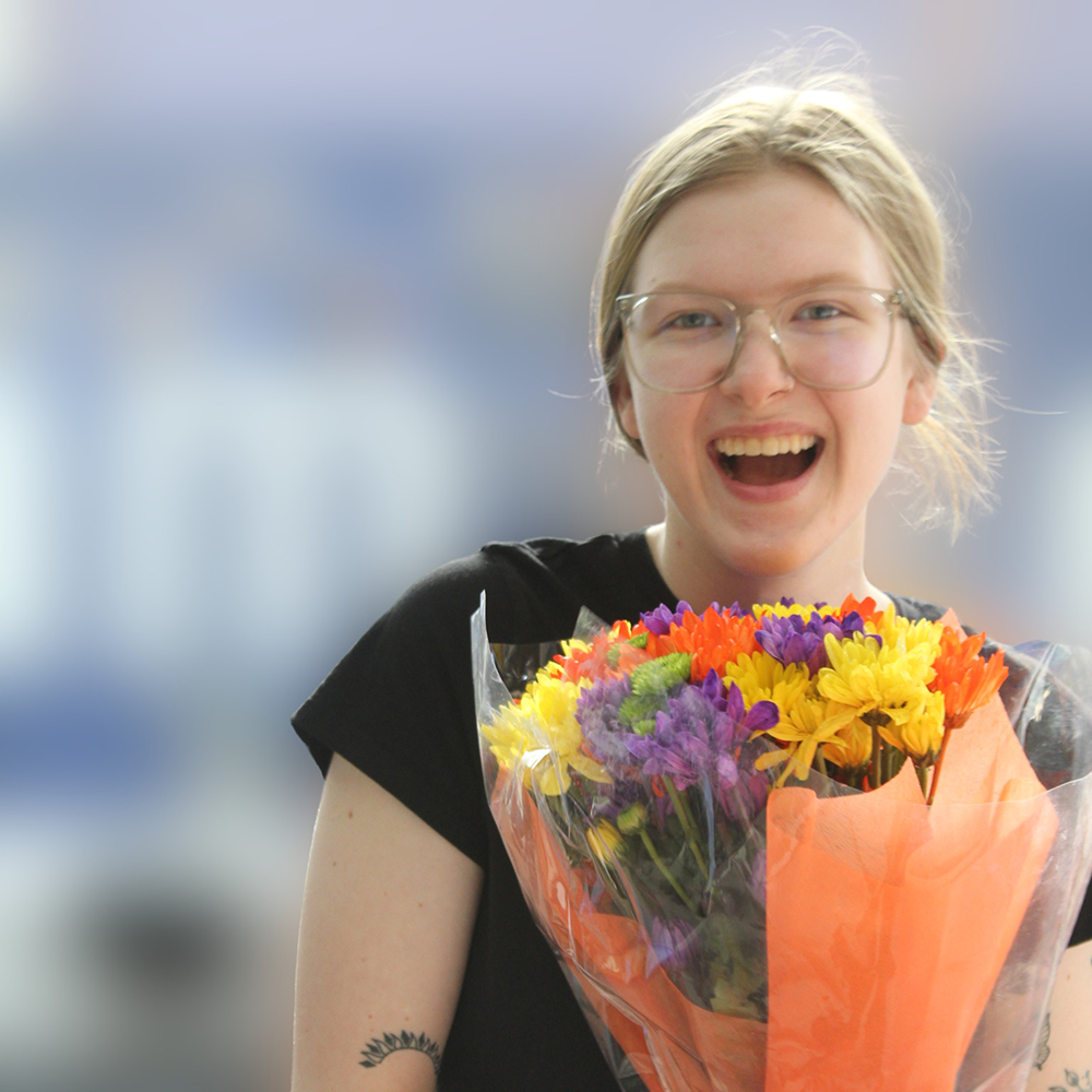 A smiling person wearing glasses holds a colorful bouquet of flowers.