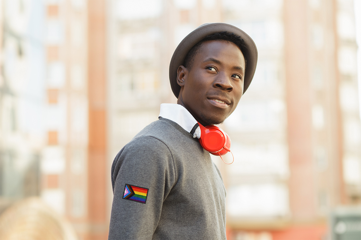 a young African American man wearing a shirt with lgbtq+ flag patch on the sleeve