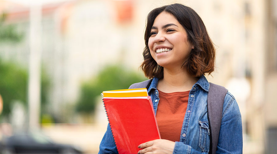young Latino female student with a backpack holding notebooks and smiling